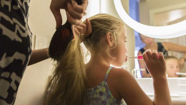 äiti kampaa tyttärensä hiuksia harjaessaan hampaitaan